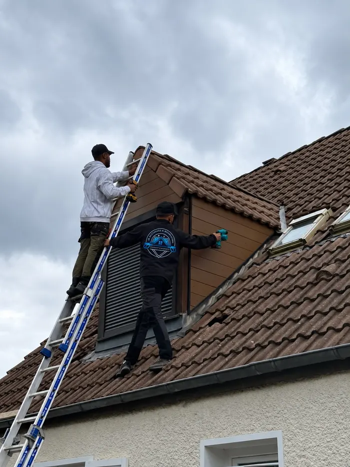 Deux couvreurs sur un toit de tuiles, l'un sur une échelle, l'autre à côté d'une lucarne