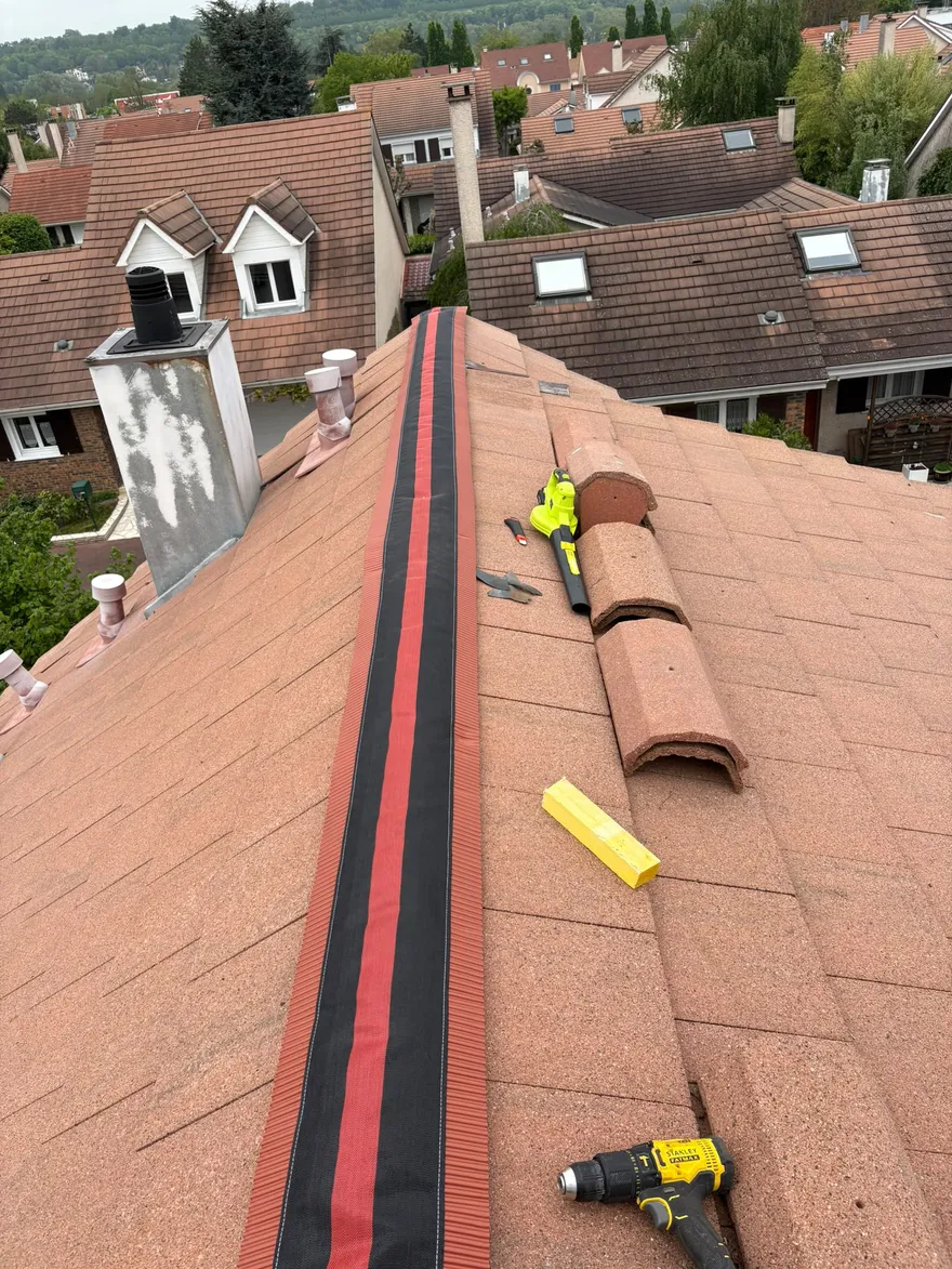 Faîtage de toiture avec un closoir noir et rouge neuf, tuiles faîtières prêtes à être reposées, vue sur les toits du quartier