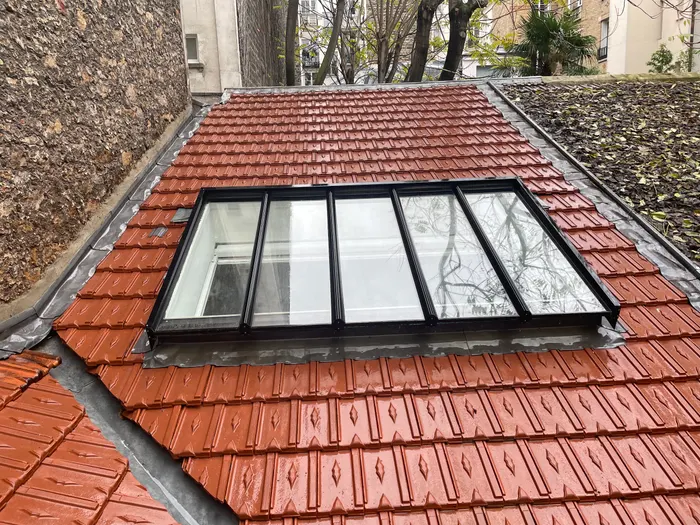 Toiture en tuiles rouges avec une verrière à cadre noir encastrée